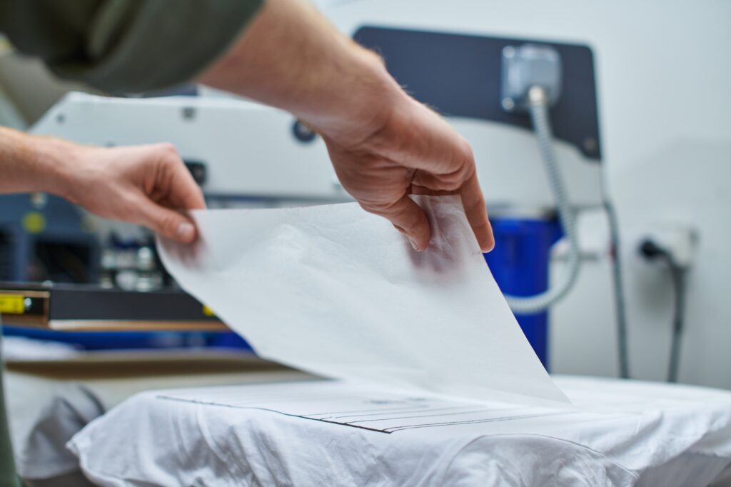 Cropped view of young craftsman putting layer on t-shirt and working on screen printing machine